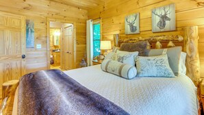 A wooden cabin bedroom with a bed, pillows, and wall art. - 2 Queen Suites, Trail Access, Mtn View, Fire Table (Blue Ridge)