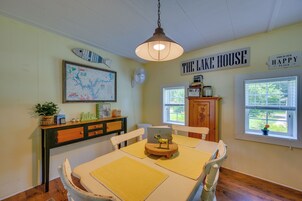 Ruokailutila, jossa on pöytä, tuoleja, seinällä kartta, kyltti, jossa lukee ”THE LAKE HOUSE”, ja ikkuna, josta avautuu näkymä vehreään maisemaan.
