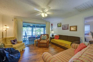 A cozy living room with a brown leather armchair, a yellow sofa, and a striped couch. There is a ceiling fan, a window with curtains, and a view of a dock. - Lake Sinclair 'crooked Creek Cottage' w/ Fire Pit! (Eatonton)