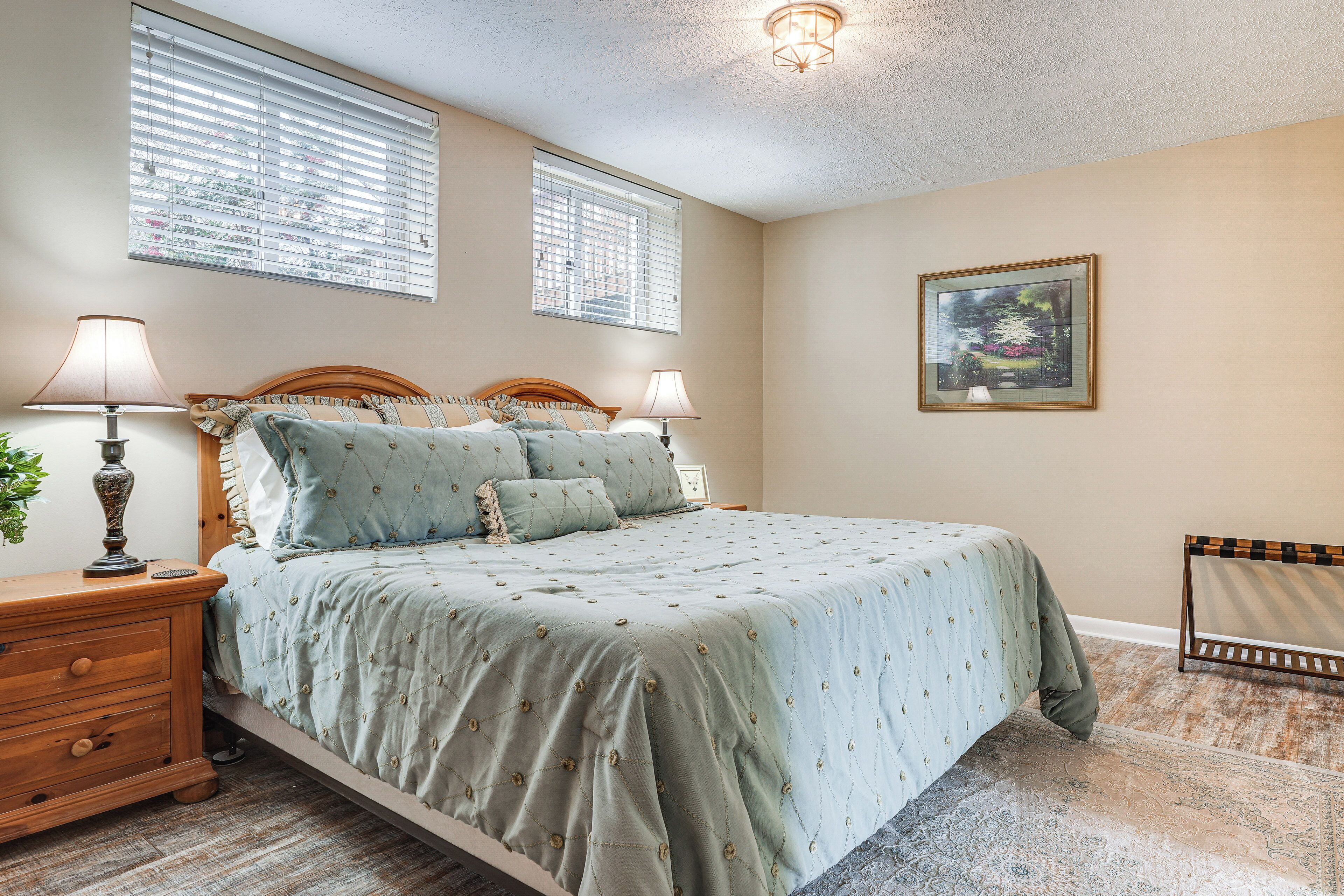 A bedroom with a bed, two bedside lamps, a nightstand, a framed picture on the wall, and a window with blinds.