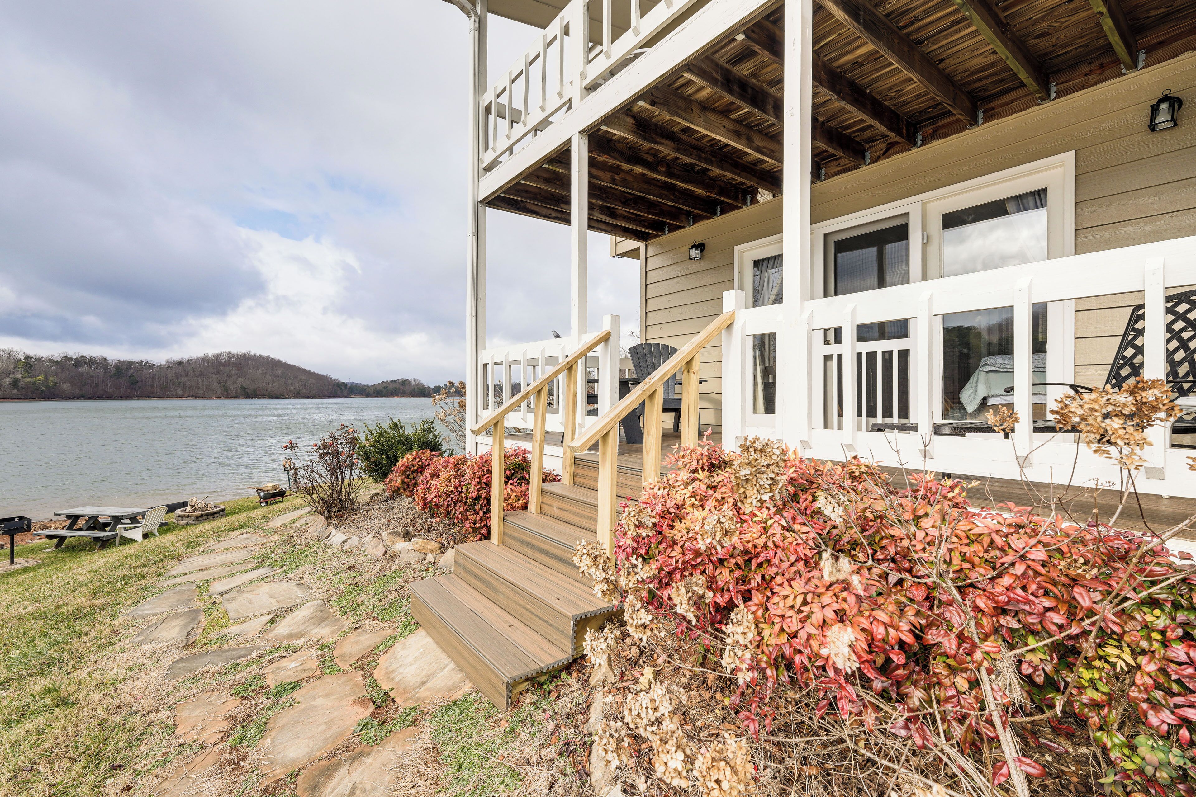 Un chalet au bord du lac, doté d’une terrasse en bois, d’un escalier en pierre et offrant une vue sur le lac.