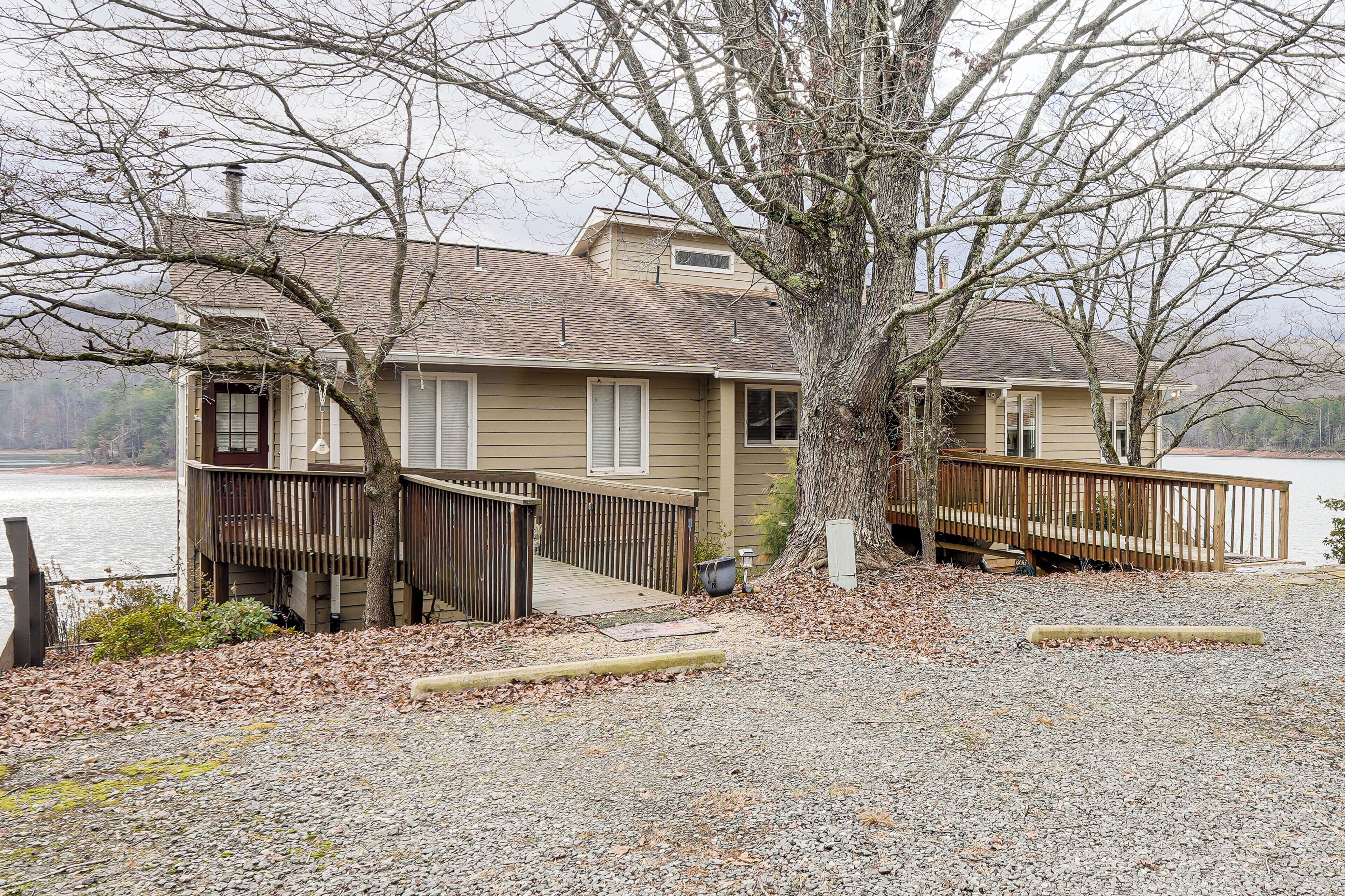 A house with a dock, a wooden deck, and a gravel driveway.