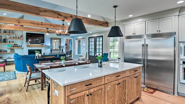 Une cuisine moderne avec des meubles en bois, un grand îlot central, des appareils en acier inoxydable et des luminaires suspendus.