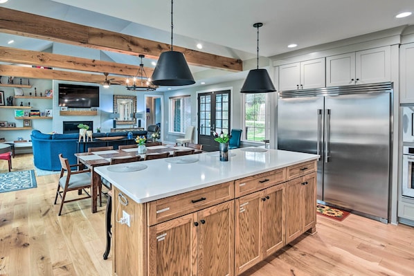A modern kitchen with wooden cabinets, a large island, stainless steel appliances, and pendant lighting.