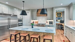 Une cuisine moderne dotée d’appareils électroménagers en acier inoxydable, d’un îlot central avec des tabourets, d’un éclairage suspendu et d’une décoration murale sur le thème du sport.