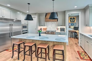A modern kitchen with a central island, stainless steel appliances, and wooden bar stools.