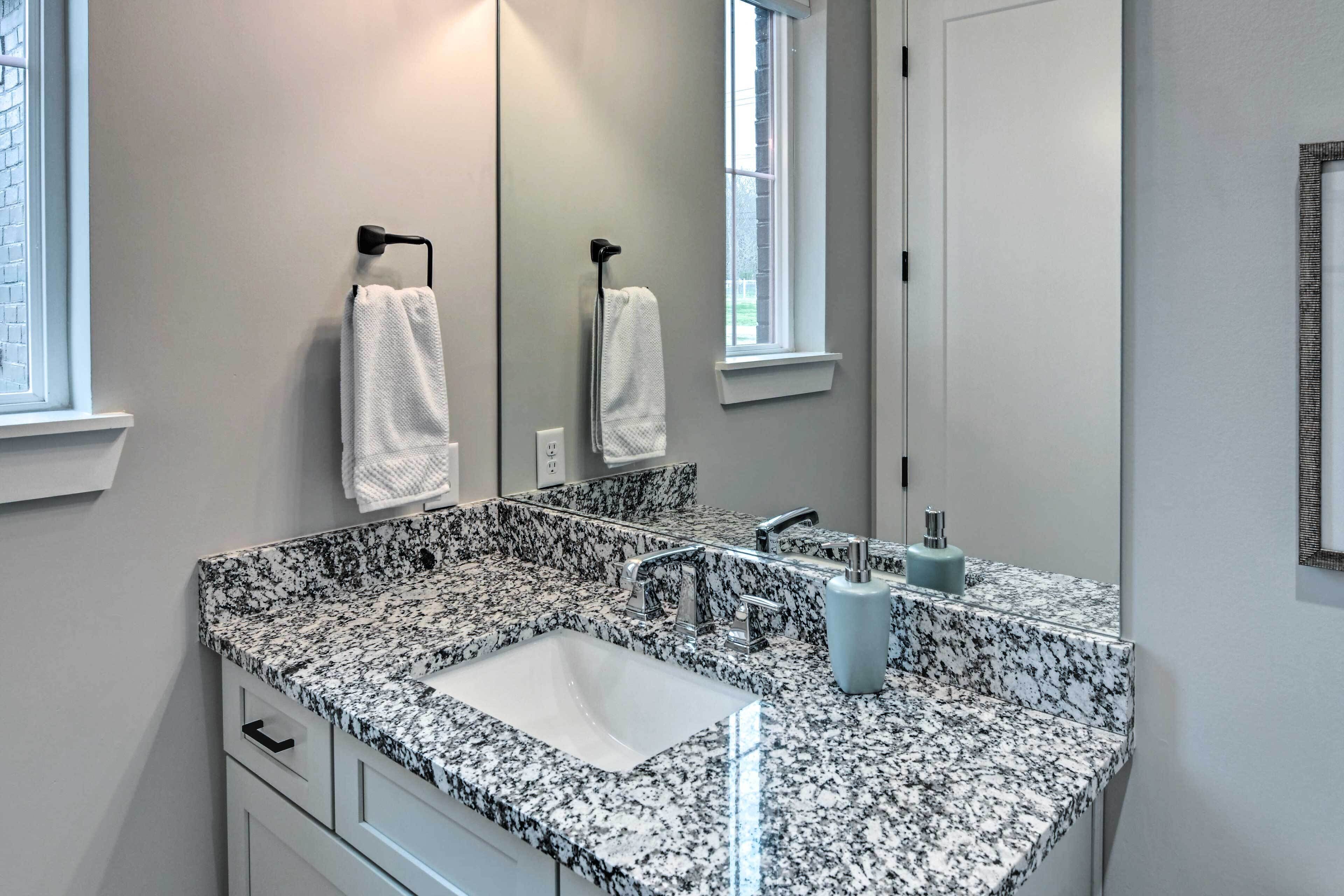A bathroom with a granite countertop sink, a mirror, and two towels hanging on hooks.