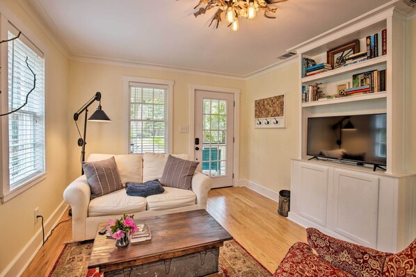 A living room with a white sofa, a coffee table, a bookshelf, and a television. - Savannah Cottage - 5 Mi to Wormsloe Historic Site! (Savannah)
