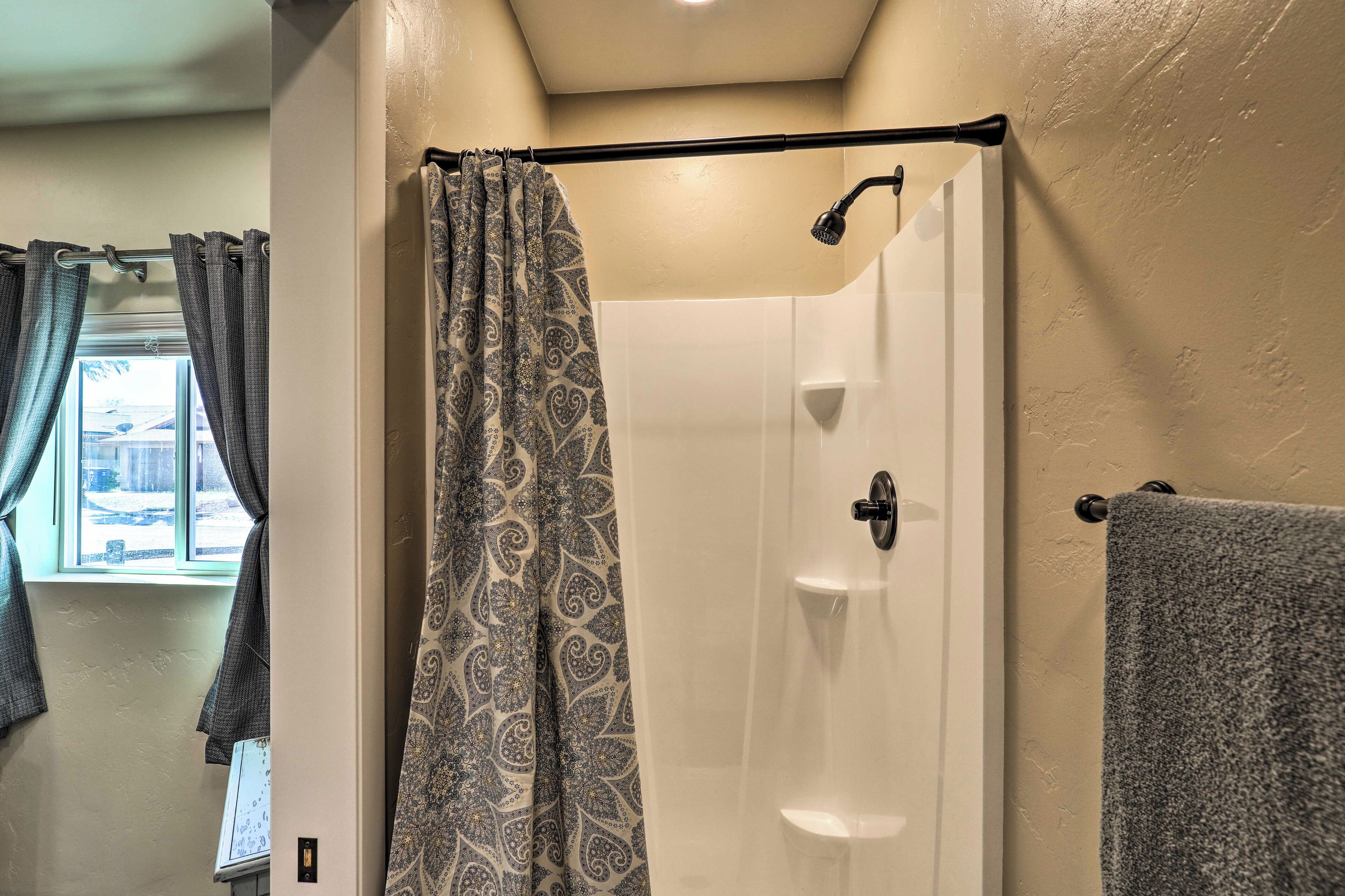 A bathroom with a shower, a towel rack, and a window with curtains.