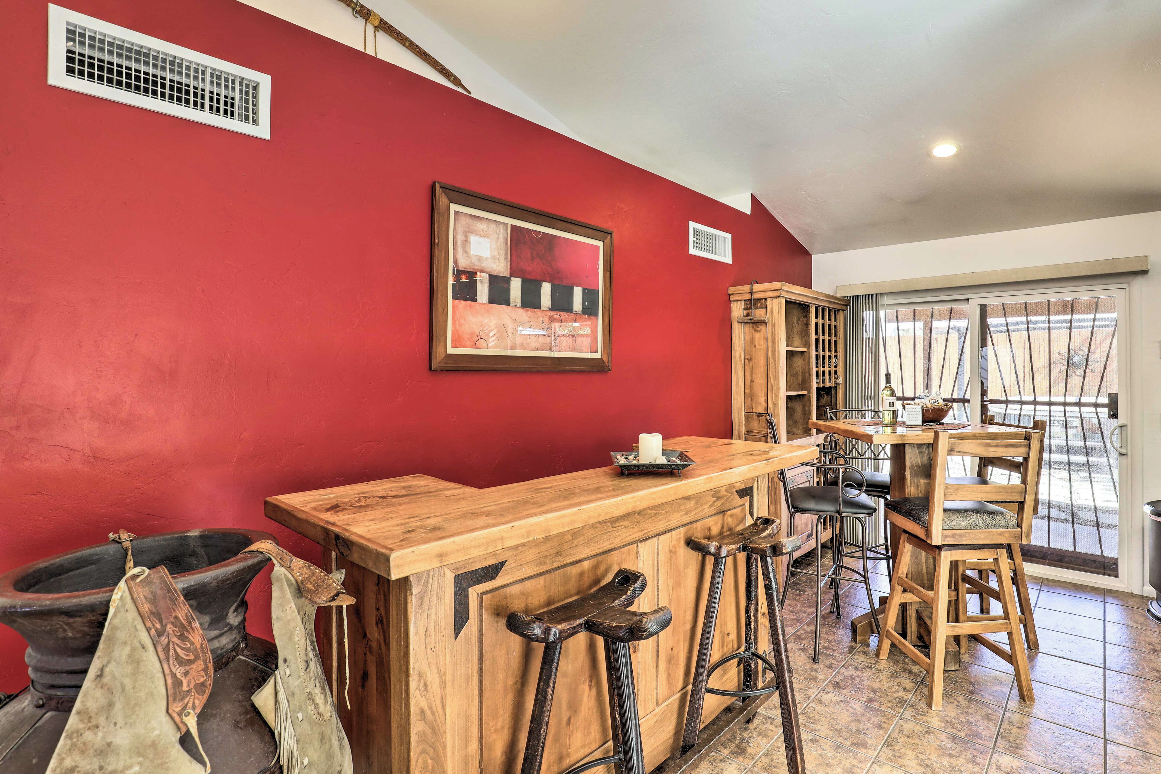 A kitchen with a red wall, wooden bar counter, stools, and a framed picture.