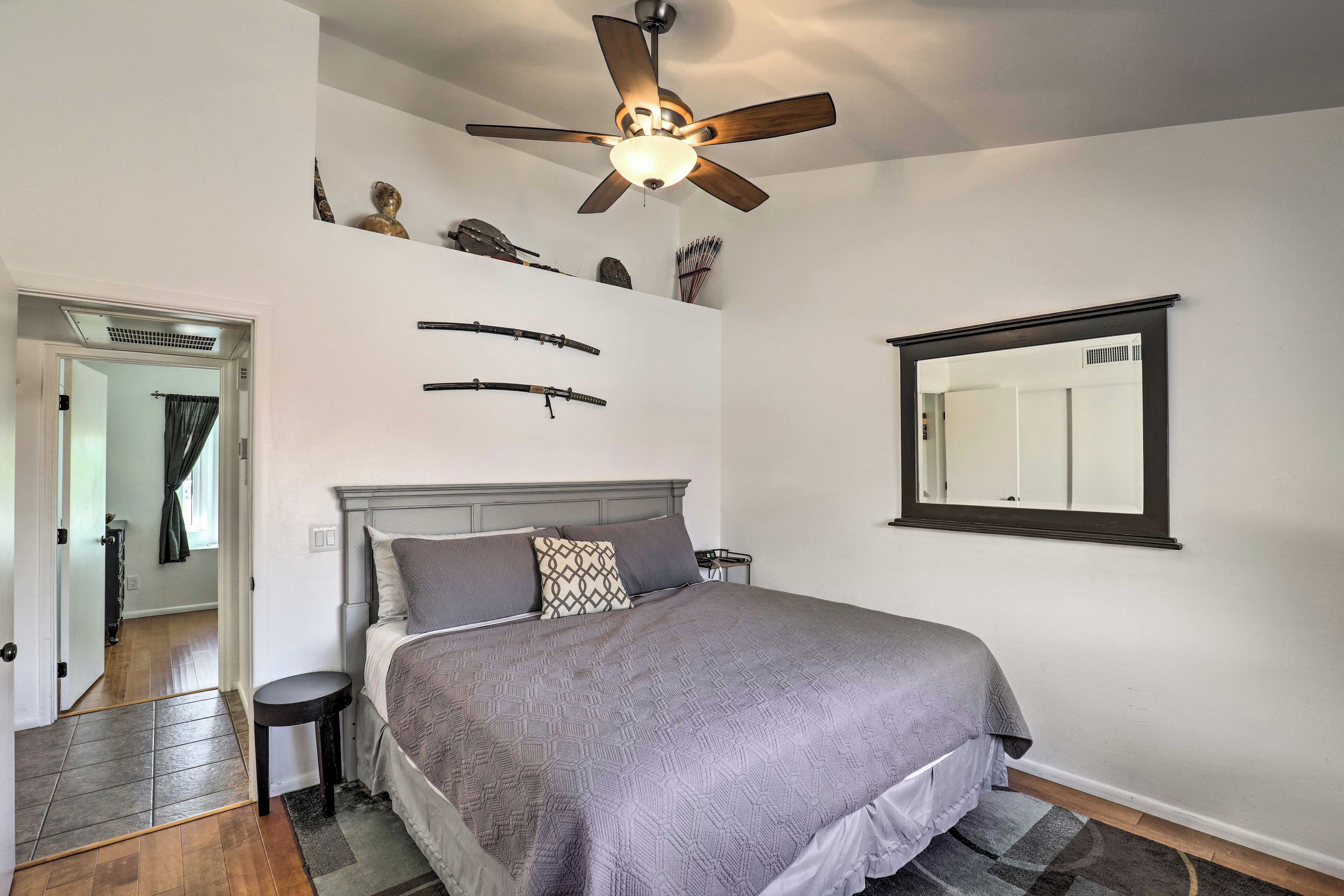 A bedroom with a bed, a ceiling fan, a mirror, and a door leading to another room.