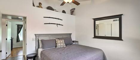 A bedroom with a bed, a ceiling fan, a mirror, and a door leading to another room.