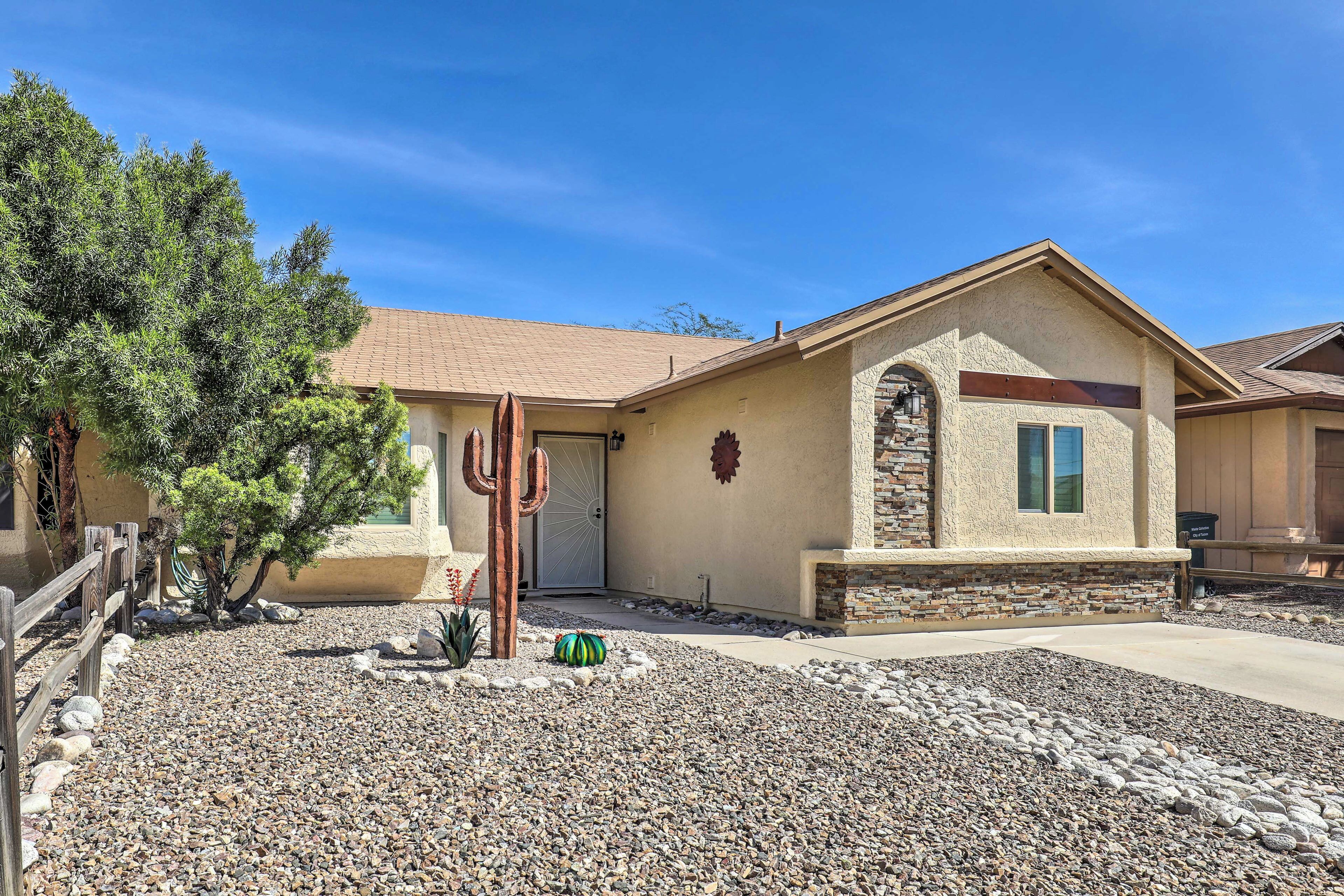 A house with a stone facade, a cacti sculpture, and a small tree in the front yard.