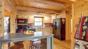 A wooden cabin kitchen with a central island, bar stools, a refrigerator, and a microwave. - Lake Blue Ridge Cabin by the Chatahoochie Forest (Blue Ridge)