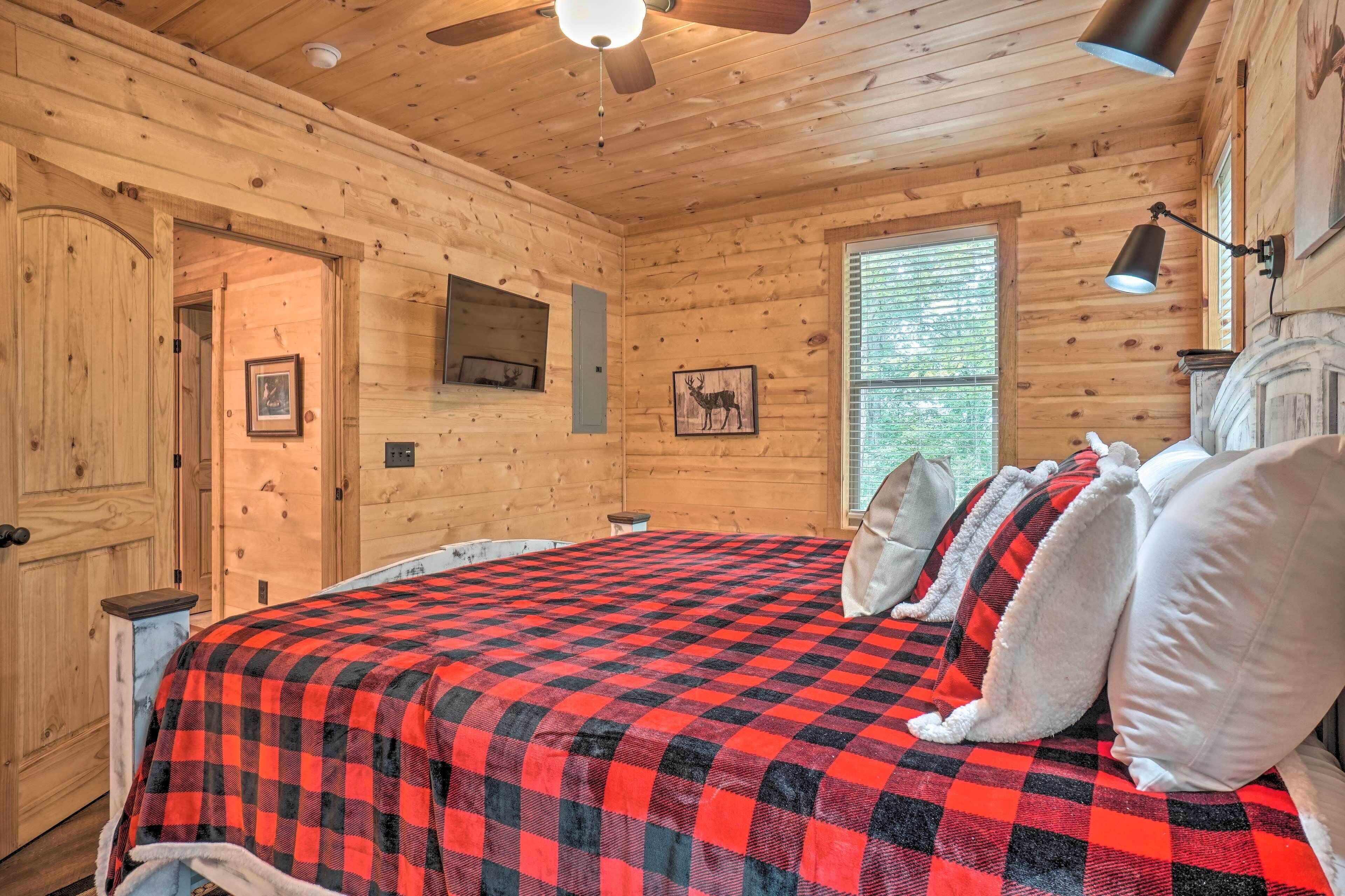 A wooden cabin bedroom with a bed, a ceiling fan, a window, and a mounted TV.