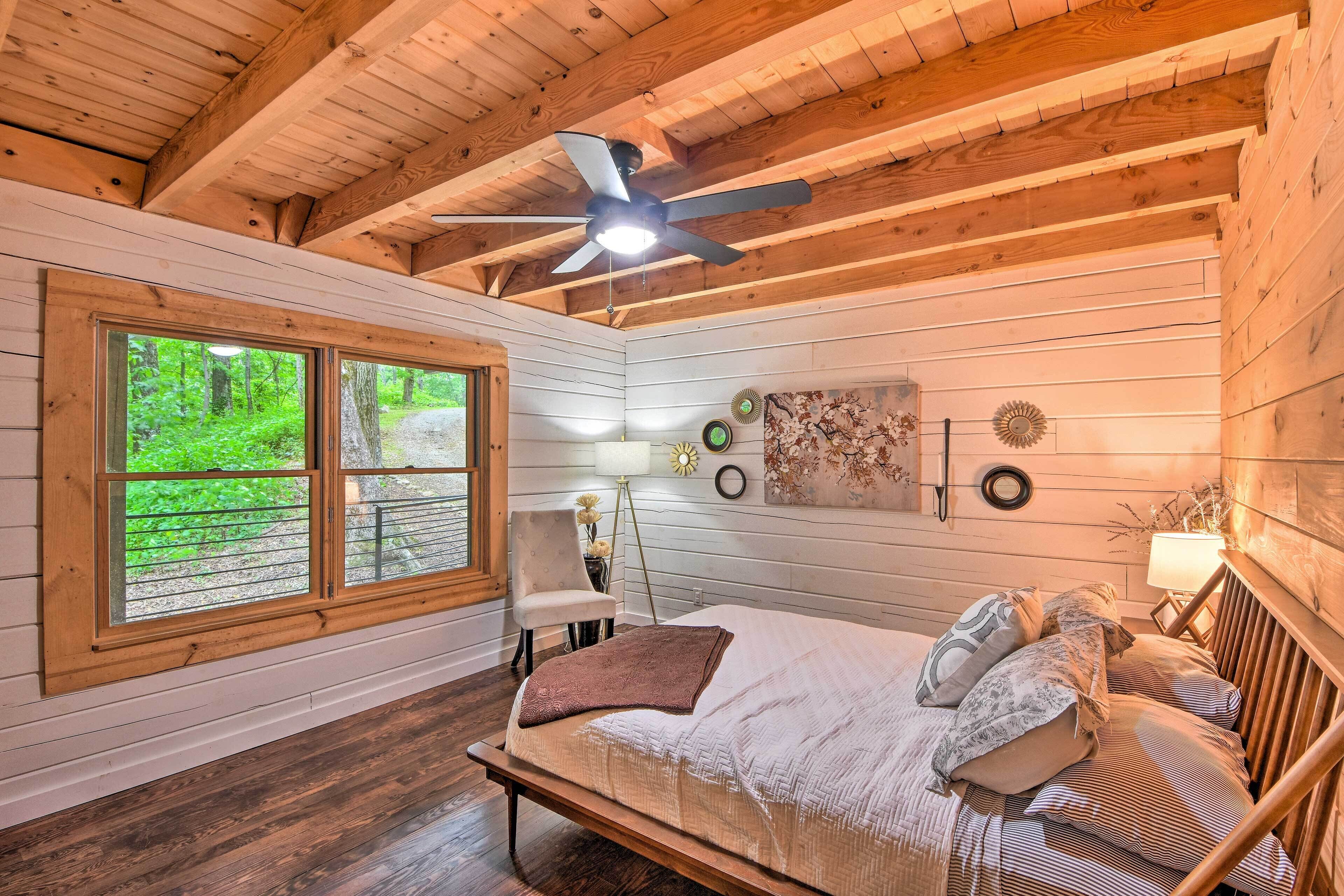 Een gezellige slaapkamer met een houten plafond, een bed met kussens, een stoel en een raam met uitzicht op groen.