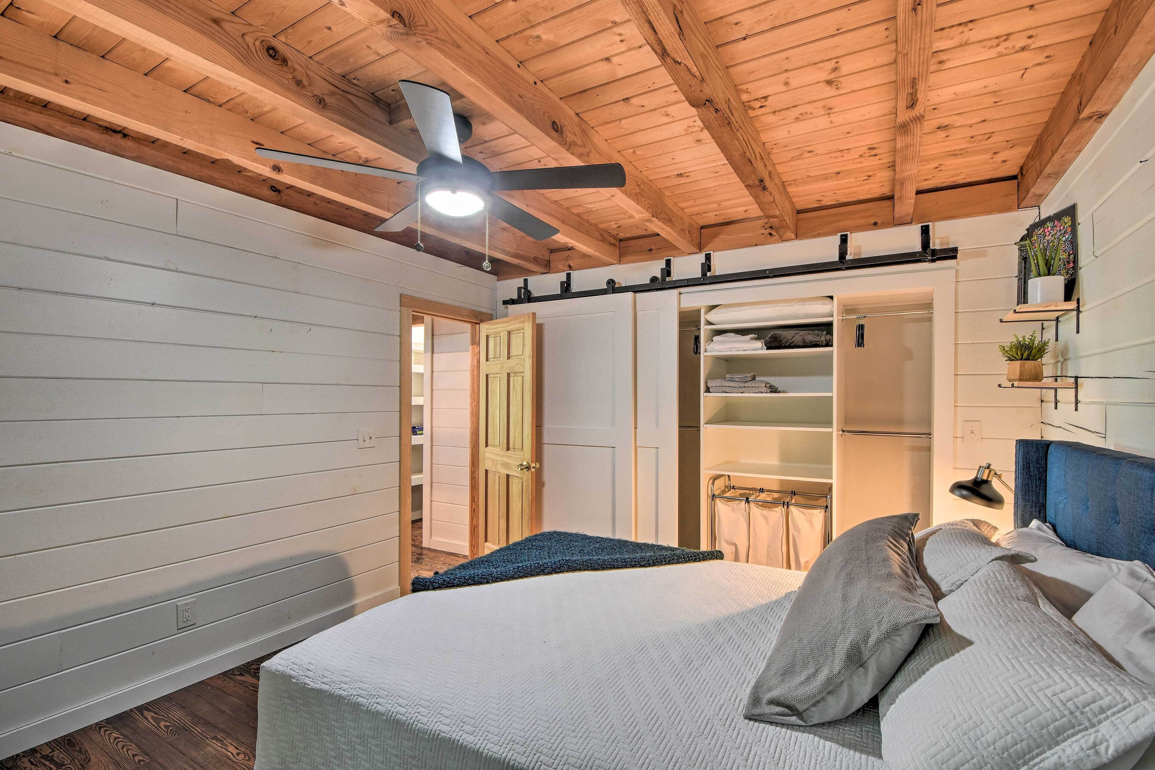 Un dormitorio con una cama, un ventilador de techo, un armario y una estantería con una planta.