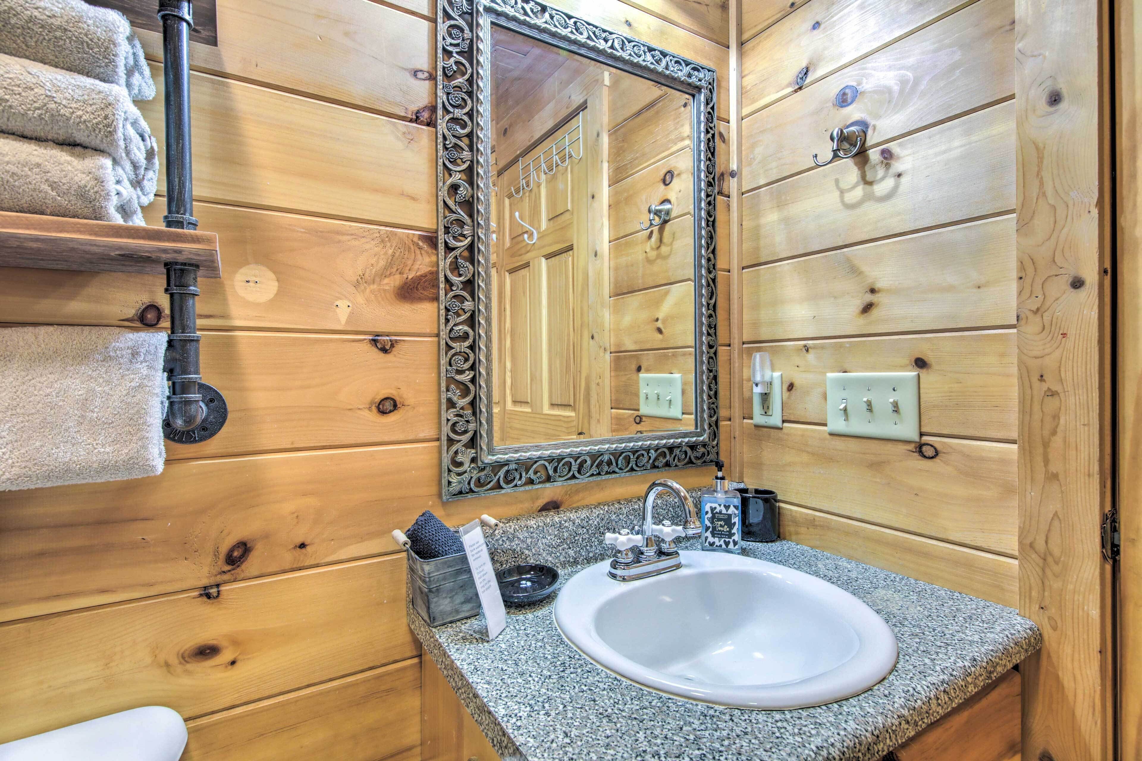Baño de cabaña de madera con lavamanos de encimera de granito, un espejo grande y un perchero para toallas.