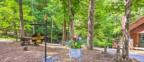 A rustic cabin with a wooden deck, surrounded by a forest. A metal sign with "Kings Court" is visible.