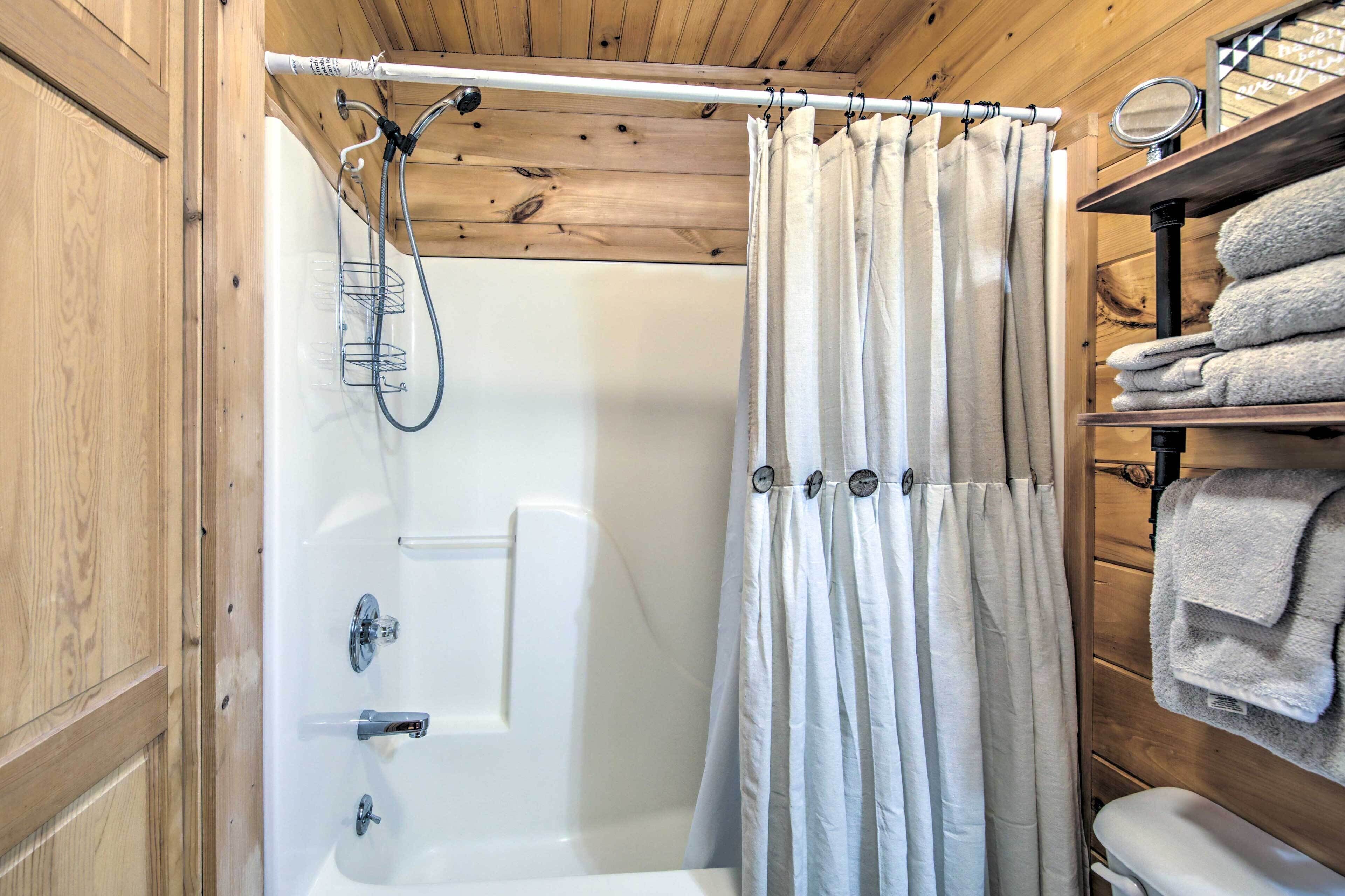 A wooden cabin bathroom with a shower, a towel rack, and a shelf with towels.