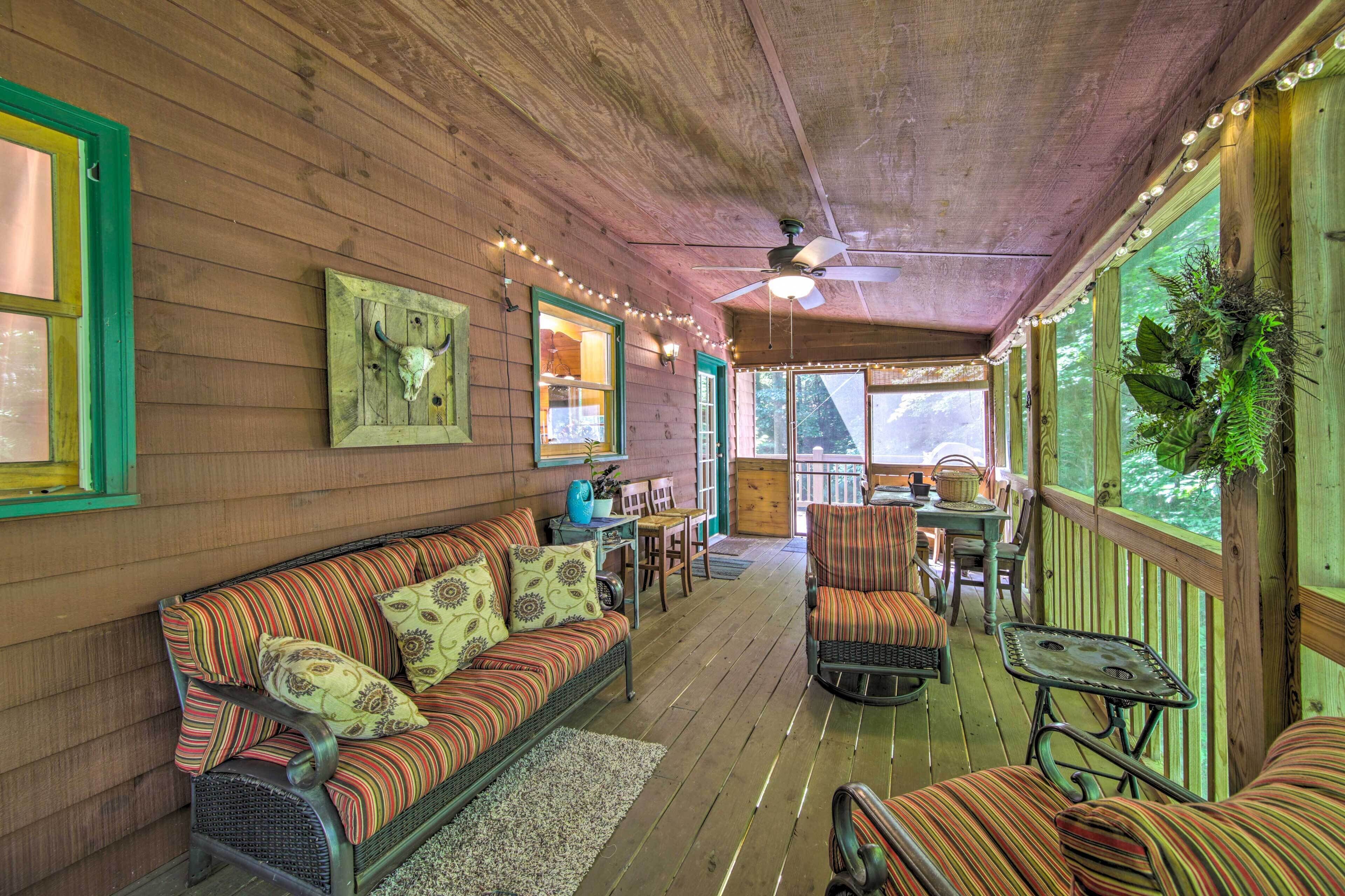 A cozy wooden cabin interior with a sofa, chairs, a dining table, and a ceiling fan.