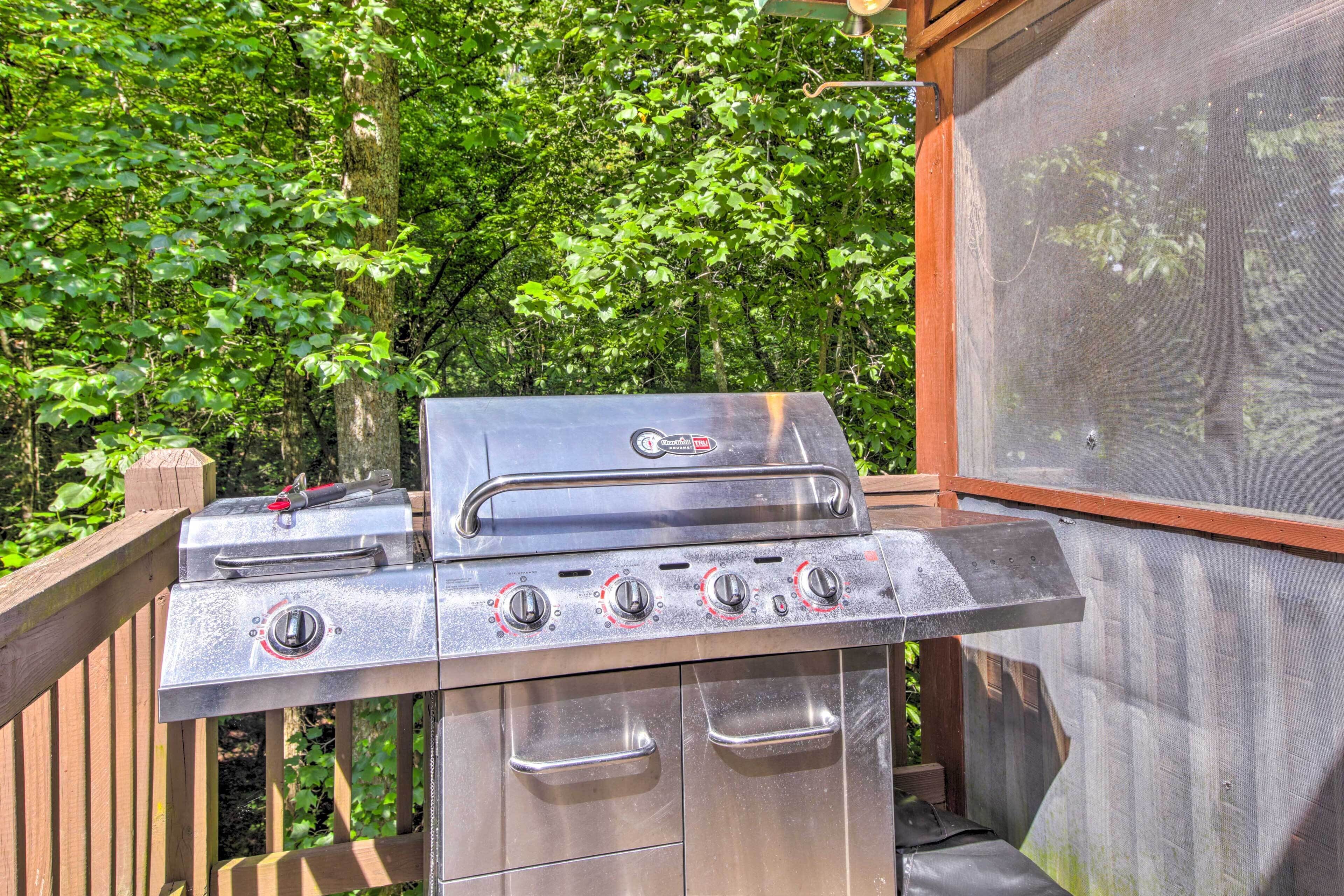 Un barbecue en acier inoxydable doté de quatre brûleurs et d’un meuble latéral, installé sur une terrasse en bois offrant une vue sur une zone boisée.