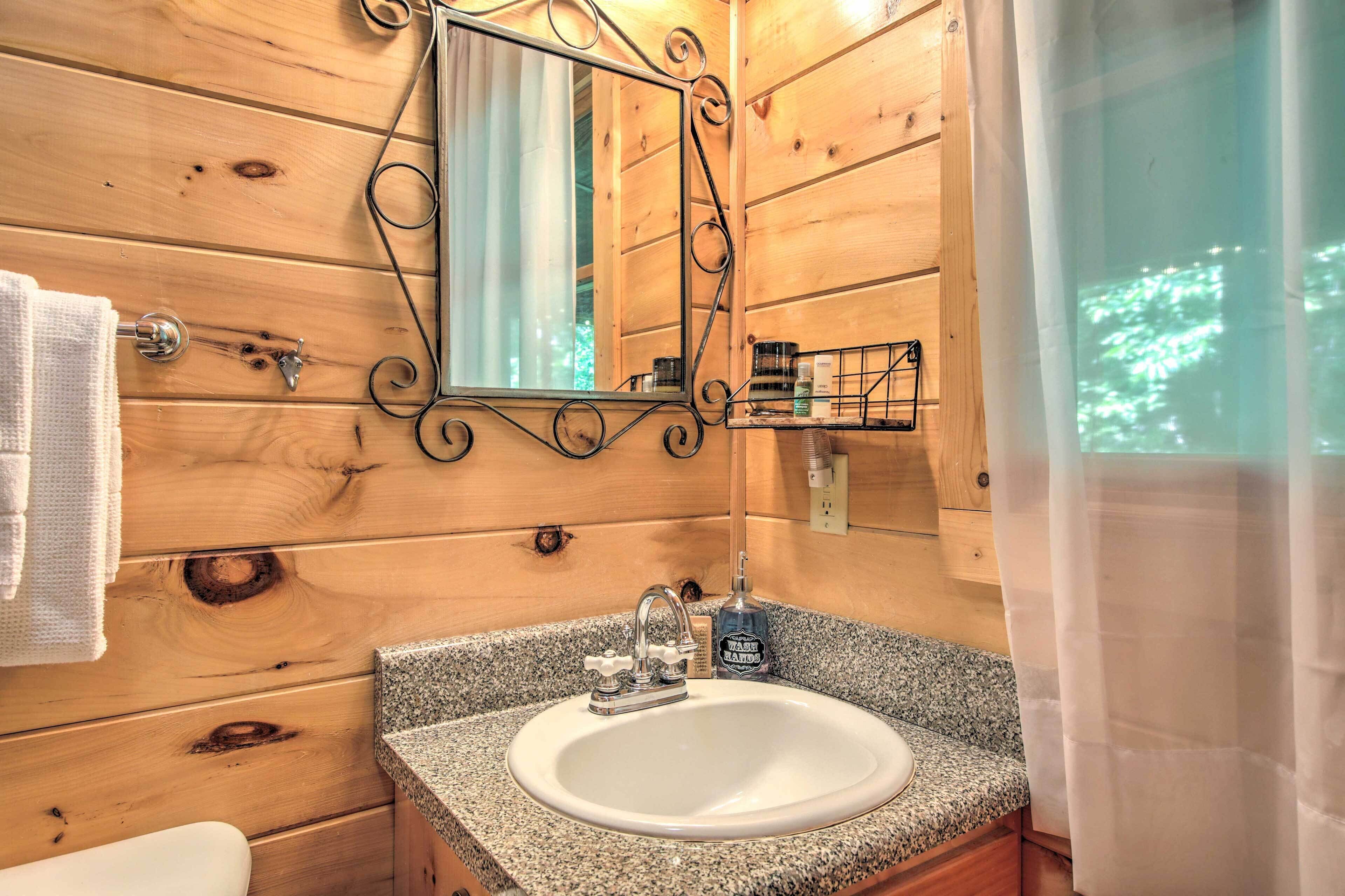 A wooden cabin bathroom with a granite countertop sink, a mirror with a decorative frame, and a window with a view of trees.