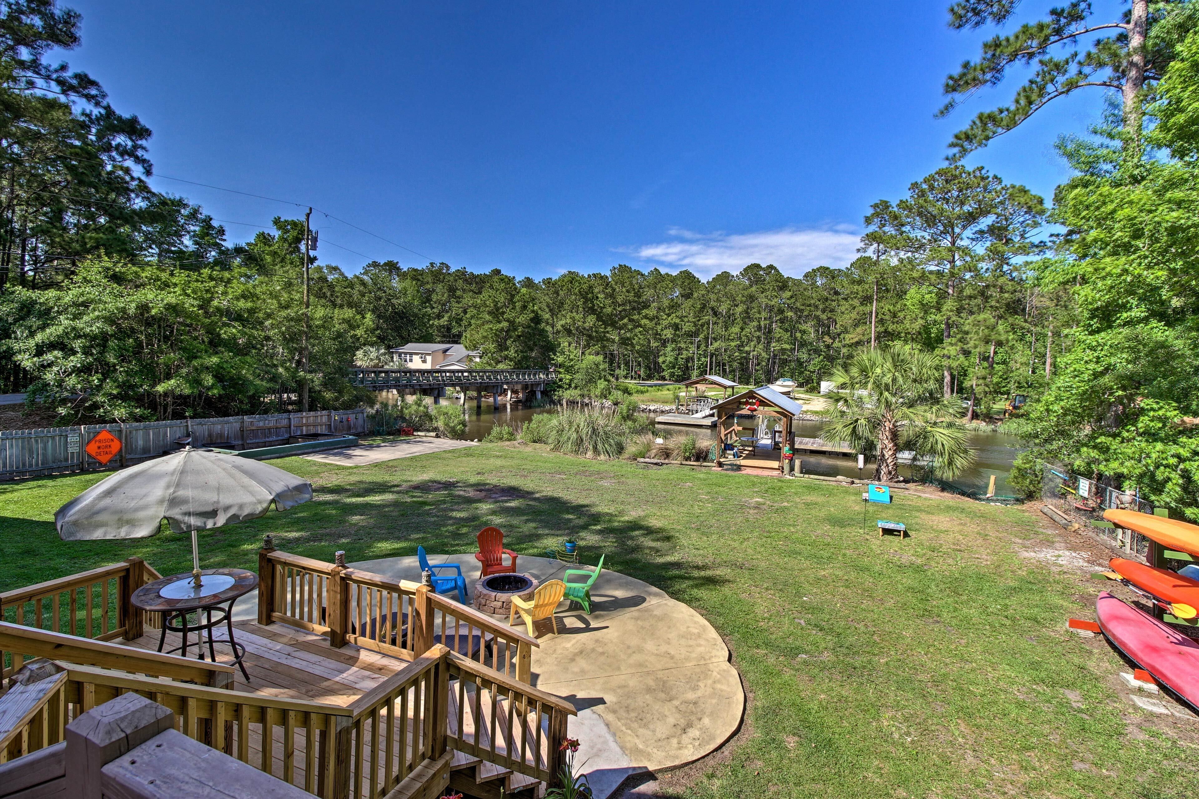 A backyard with a wooden deck, outdoor seating, a fire pit, and a pond.