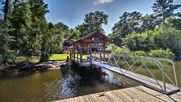 A dock holiday area with a wooden deck and a covered seating area overlooking a body of water, surrounded by lush greenery.