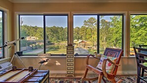 A room with large windows, a wooden rocking chair, a desk with a typewriter, and a tall chest of drawers.
