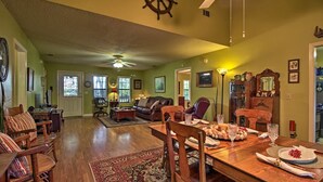 A spacious living room with a wooden dining table set for a meal, a cozy seating area with a sofa and chairs, and a kitchen visible in the background.
