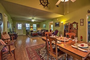 Un salón espacioso con una mesa de comedor de madera dispuesta para una comida, una zona de estar acogedora con un sofá y sillones, y una cocina visible al fondo.
