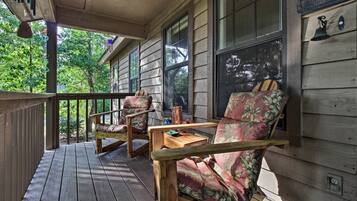 Relax on the porch with two comfortable chairs and a small table, surrounded by a serene natural landscape.