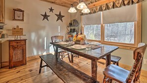 Un comedor rústico con una mesa de madera dispuesta para cuatro personas, un banco y una ventana con vistas a árboles.