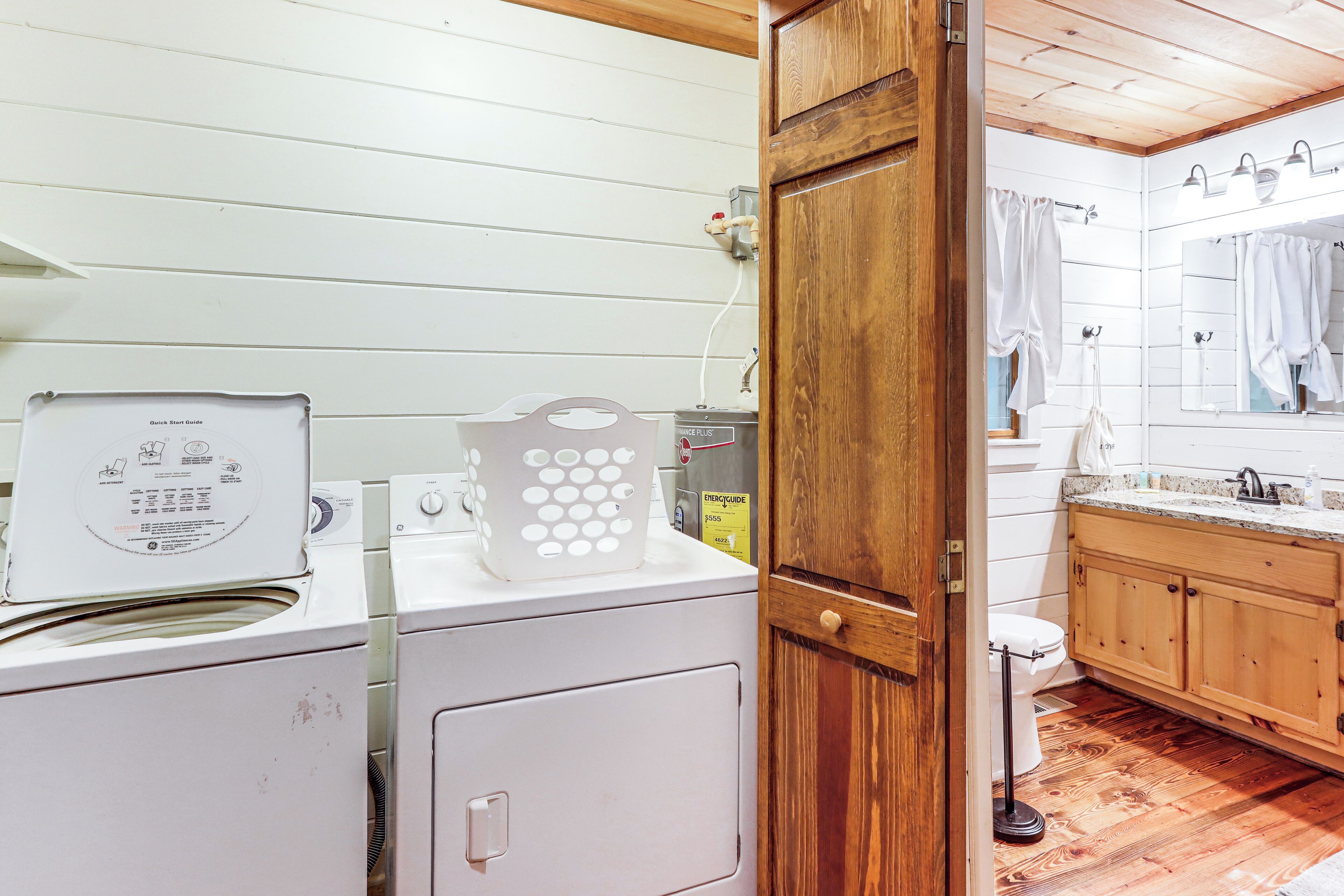 Un área de lavandería con lavadora, secadora y una puerta de madera que da a un baño.