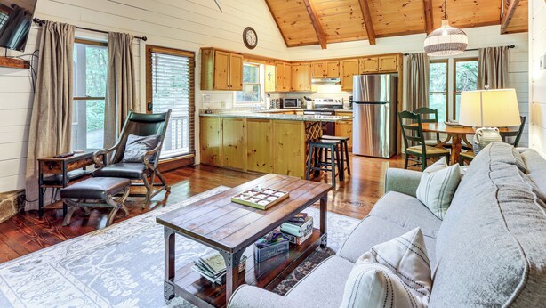 A spacious living area with a wooden ceiling, a sofa, a coffee table, and a kitchen in the background. - Creek Front Cabin w/ Hot Tub+fire Pit (Blue Ridge)