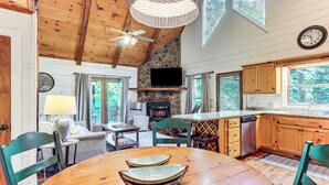 A wooden interior with a stone fireplace, wooden cabinets, and a dining table with chairs. - Creek Front Cabin w/ Hot Tub+fire Pit (Blue Ridge)