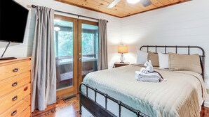 A bedroom with a bed, a TV, a wooden dresser, a lamp, and a ceiling fan. - Creek Front Cabin w/ Hot Tub+fire Pit (Blue Ridge)
