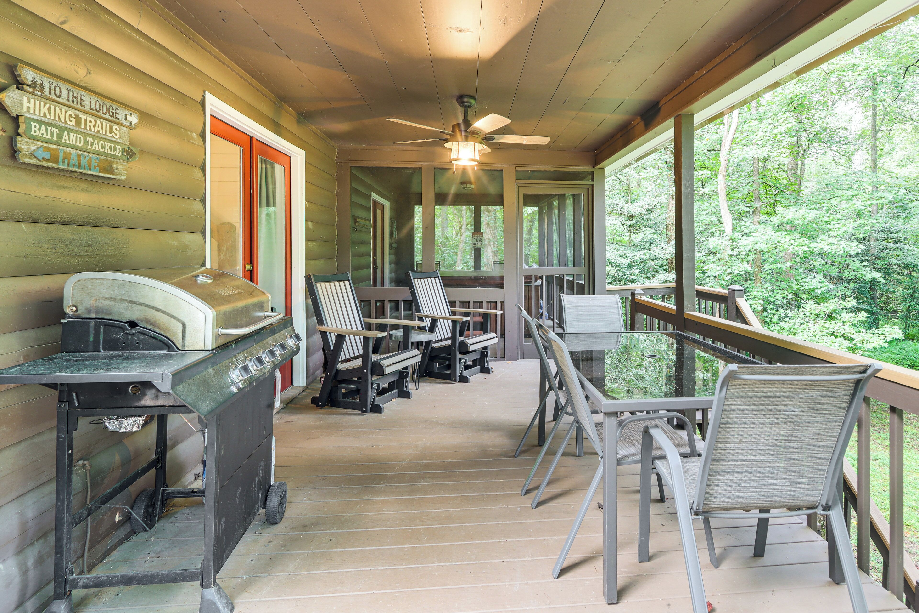 Una terraza de madera con mobiliario exterior, una parrilla y un letrero que indica senderos para caminatas y venta de aparejos de pesca.