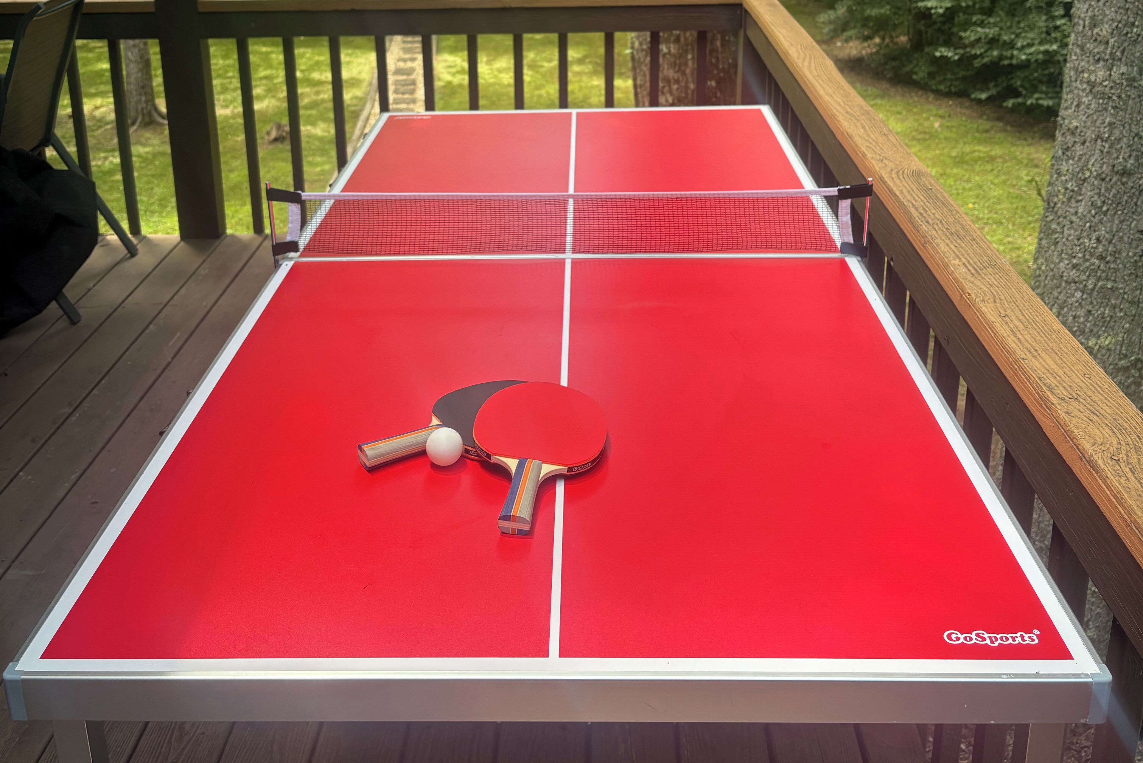 Un tavolo da ping pong rosso con due racchette e una pallina su un pontile di legno.