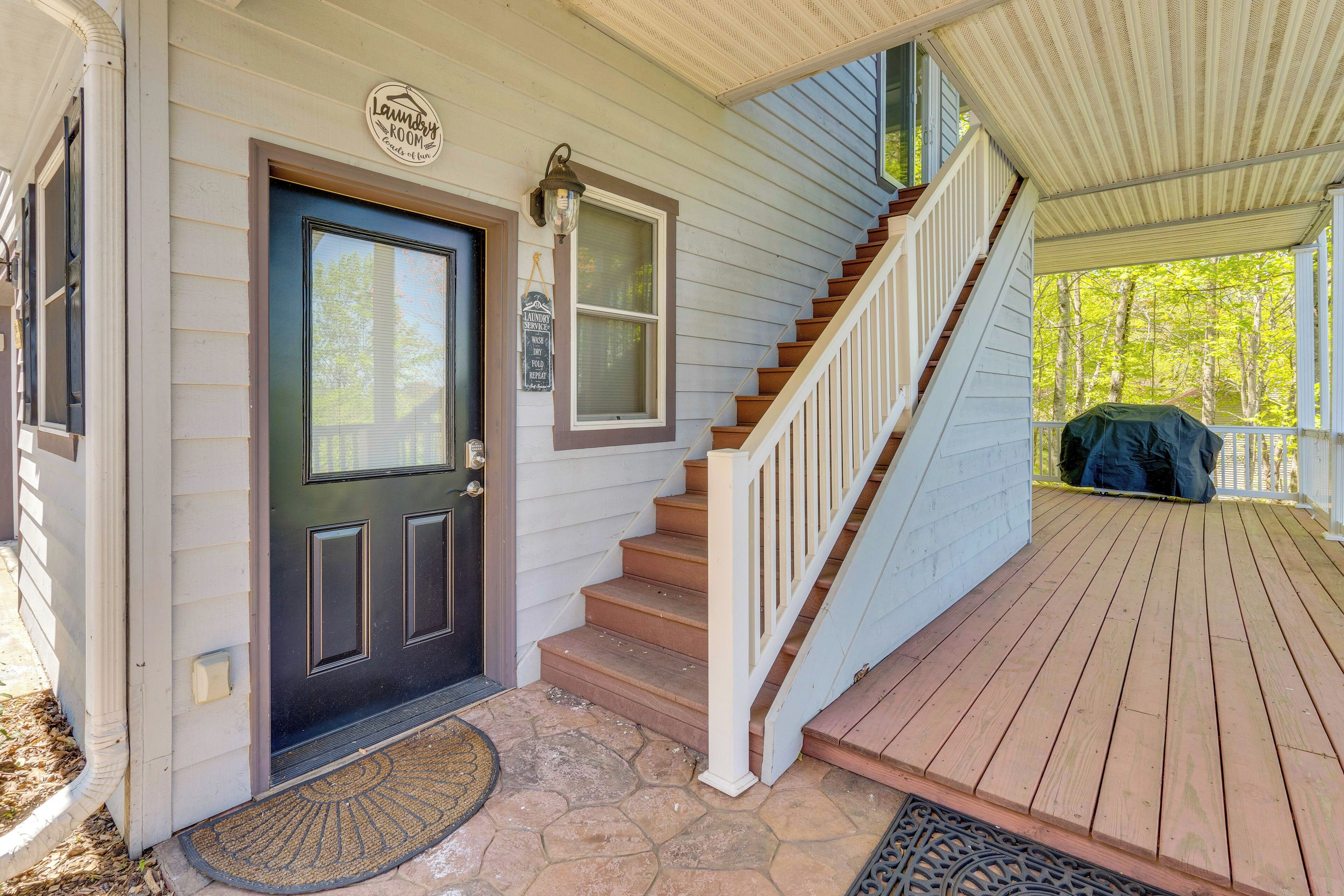 A wooden front door with a black inset panel, a small porch with a wooden staircase, and a covered area with a green tarp.
