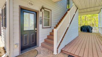 A wooden front door with a black inset panel, a small porch with a wooden staircase, and a covered area with a green tarp.