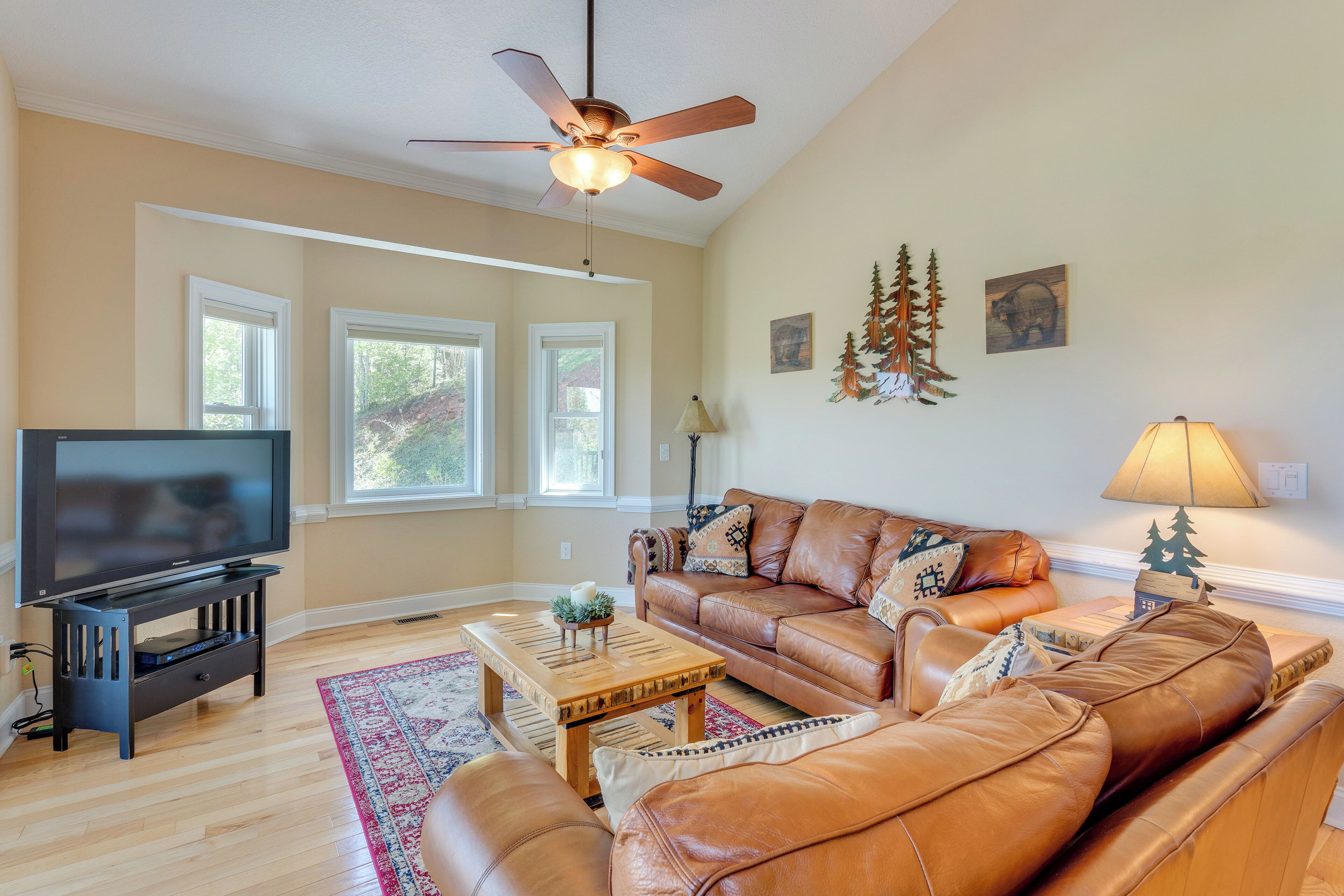 A living room with a leather sofa, a coffee table, a TV on a stand, and a ceiling fan.