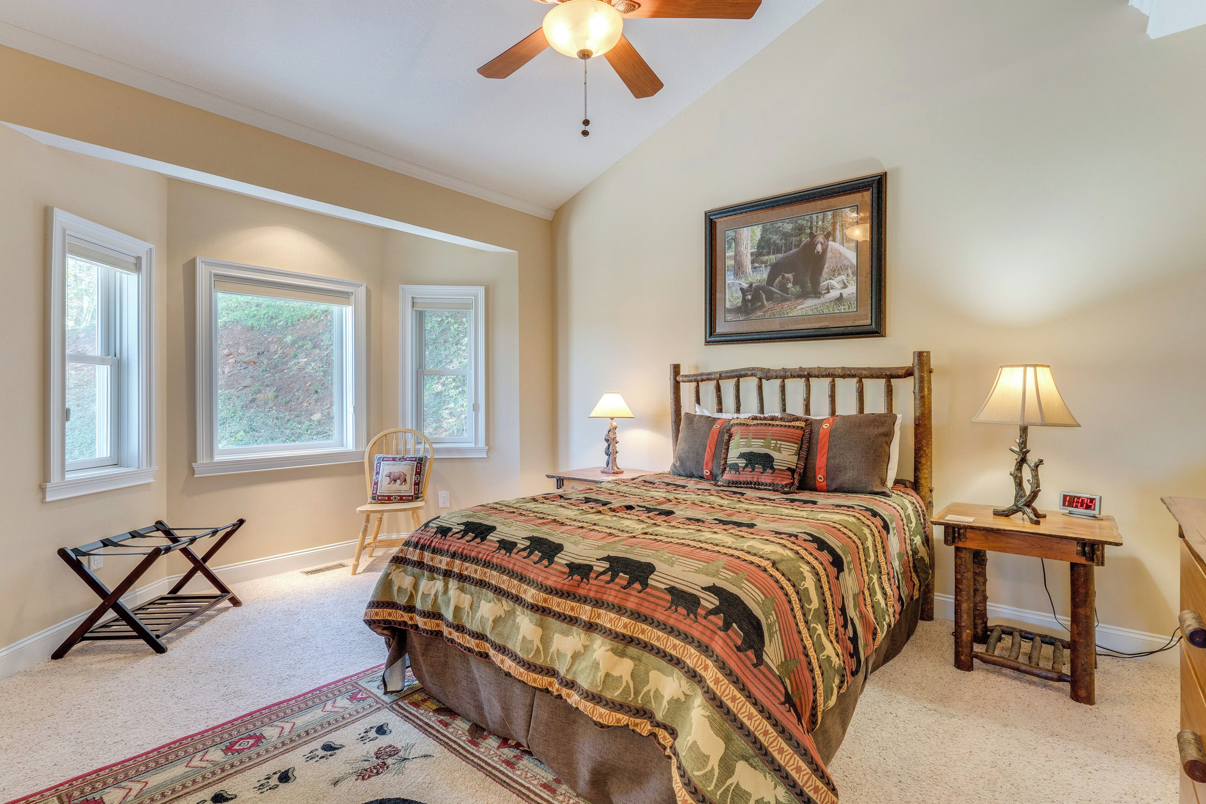 A bedroom with a large bed, two bedside tables with lamps, a ceiling fan, and a framed picture on the wall.