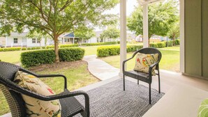 A covered porch with two wicker chairs and a small rug, overlooking a well-manicured lawn and a row of houses. - Chic Thomasville Home: Walk to Downtown! (Thomasville)