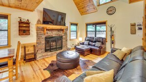 A cozy living room with a stone fireplace, leather sofas, and a wooden ceiling.