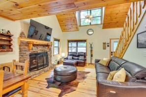 A cozy living room with a stone fireplace, leather sofa, and a dining area with wooden furniture. - Spacious Cabin w/ Deck + Hot Tub in Blairsville (Blairsville)