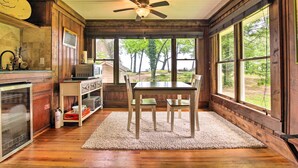 A wooden interior with a dining table, chairs, a ceiling fan, and large windows offering a view of trees.