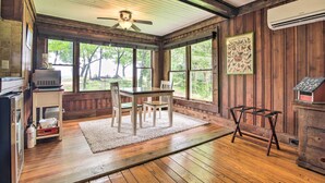 A room with wooden floors, a ceiling fan, a table with chairs, a rug, and a window with a view of trees.