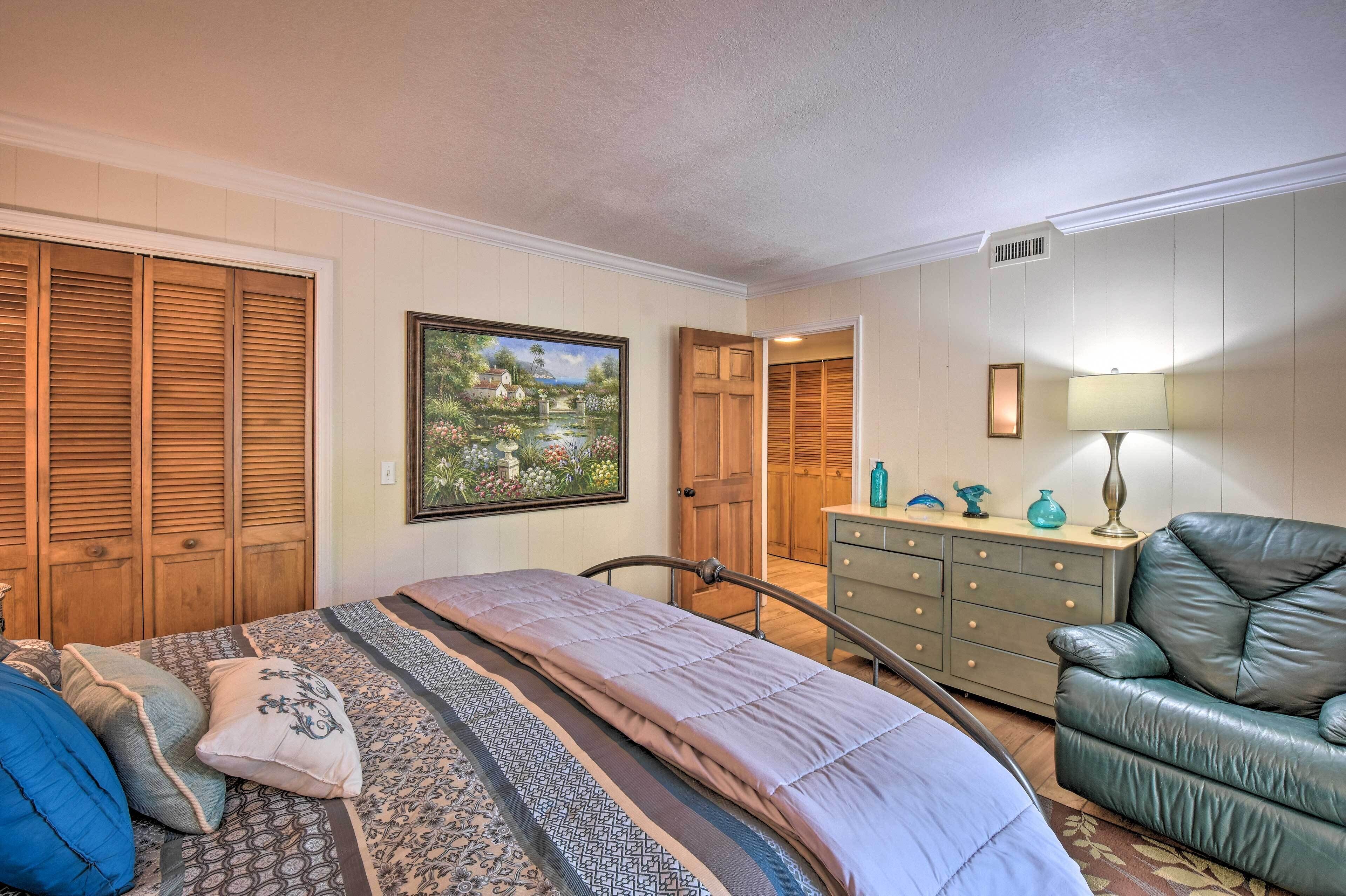 Un dormitorio con cama, cómoda, silla y un cuadro en la pared.